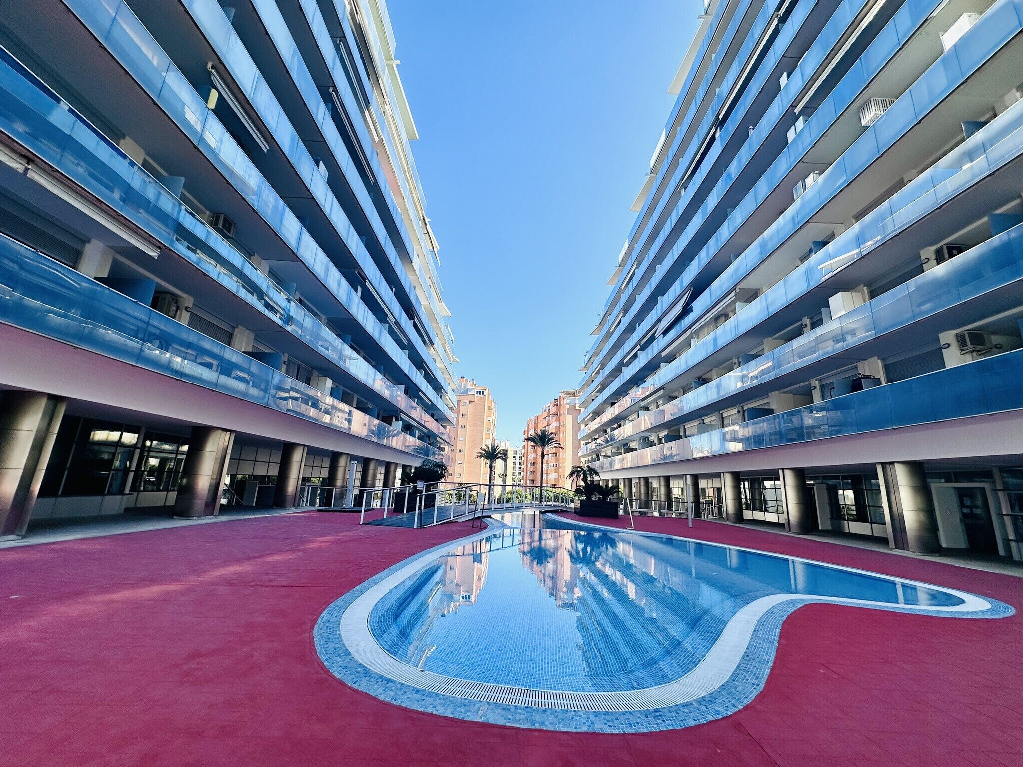 Un edificio moderno con piscina central, varios balcones y cielo despejado.