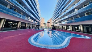 A modern building with a central swimming pool, multiple balconies, and a clear sky.
