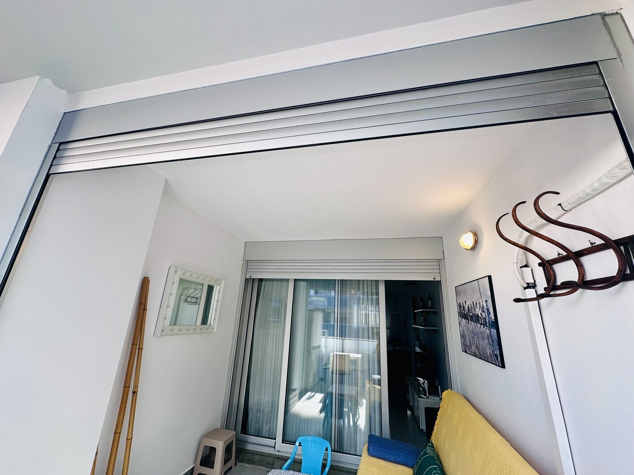 A room with a sliding door leading to a balcony, a small stool, a blue chair, and a sofa.