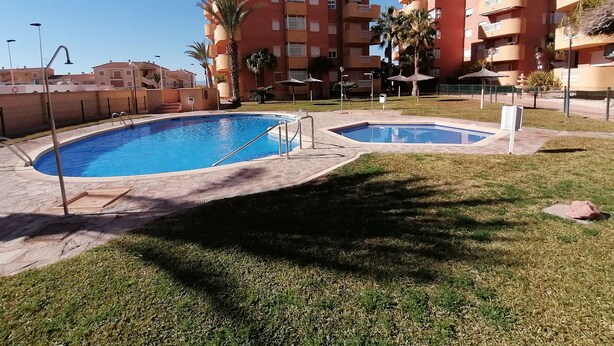 Une piscine entourée d’une pelouse, avec un immeuble à plusieurs étages en arrière-plan.
