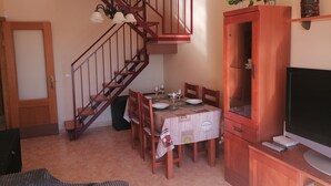 Un coin repas avec un escalier en bois, une table à manger dressée avec des assiettes et des verres, un meuble contenant un téléviseur et une petite plante accrochée au mur.