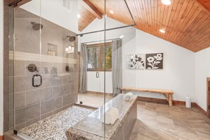 Un baño moderno con ducha de vidrio, un banco y una obra de arte en la pared.