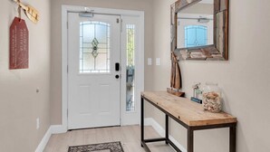 Un couloir avec une porte blanche, un banc en bois, un miroir et une enseigne décorative en bois.