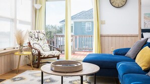 A cozy room with a blue sofa, a wicker chair, a round table, and a view of a house through a sliding door. - Steps to Beach, Pool & Tennis in heart of Corolla (Corolla)