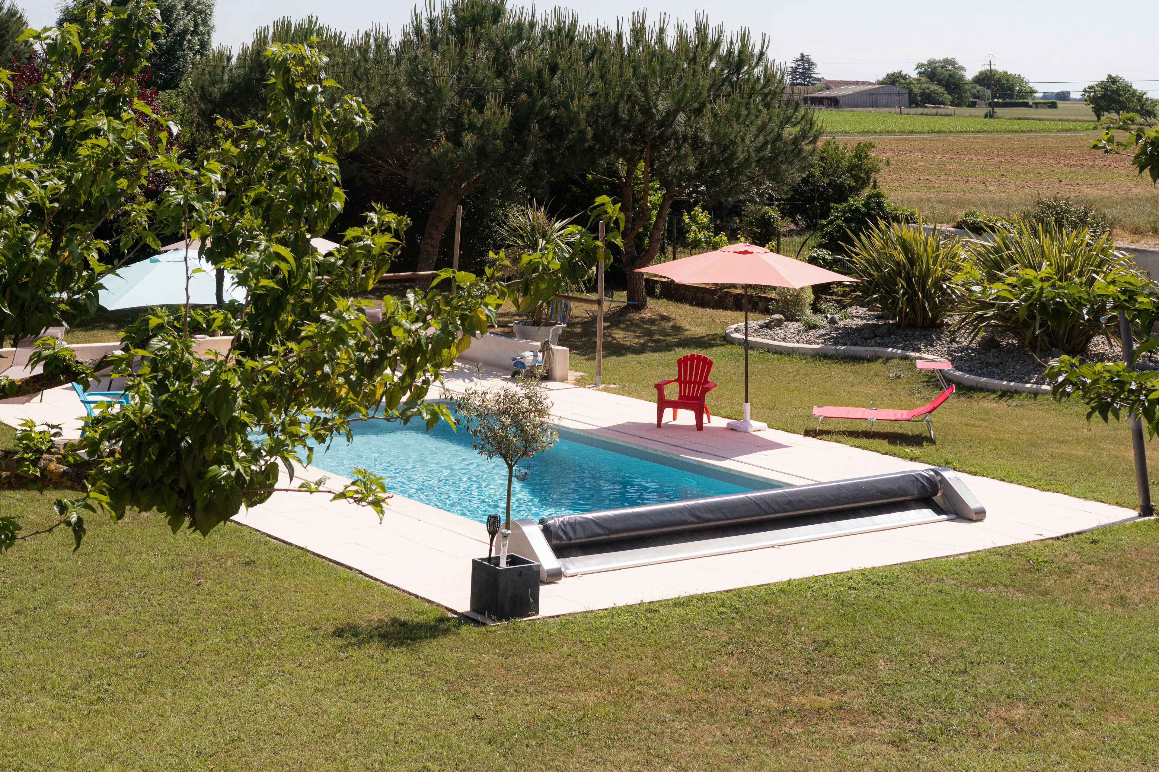 Ein Garten mit Swimmingpool, roten Liegestühlen und einer kleinen Gartenanlage.