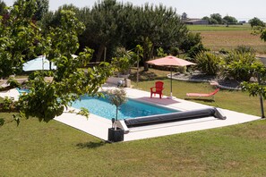 Un patio trasero con piscina, sillas reclinables rojas y un pequeño jardín.