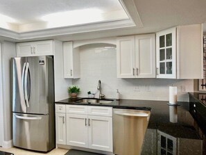 A modern kitchen with stainless steel appliances, white cabinetry, and a black countertop.