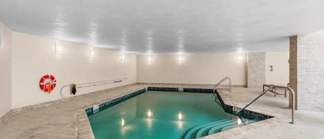 Une piscine intérieure à l’eau claire, équipée d’une bouée de sauvetage et d’une rampe d’accès pour fauteuils roulants.