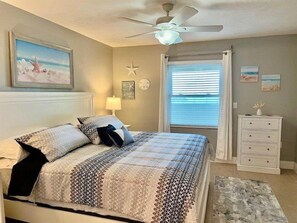 A bedroom with a bed, a ceiling fan, a window with blinds, a dresser, and wall decorations.