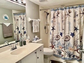 A bathroom with a sink, toilet, and shower curtain with a nautical theme.