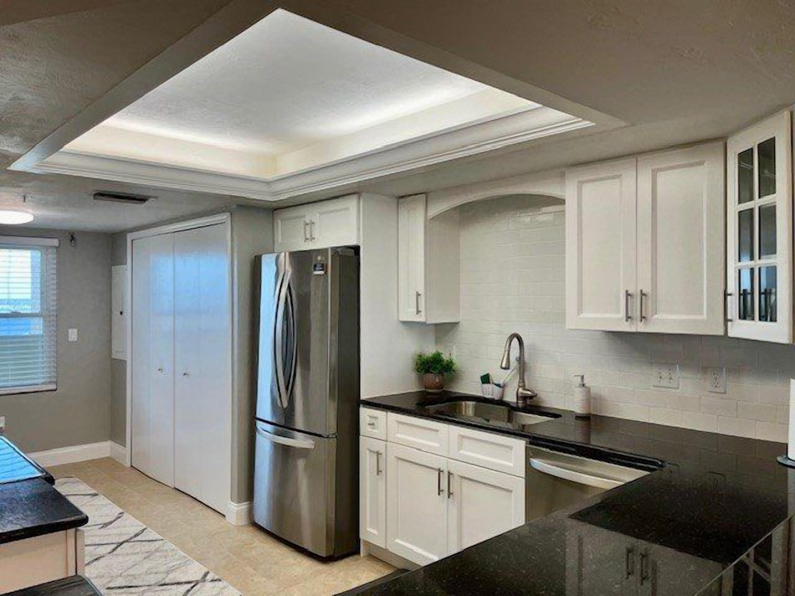 A modern kitchen with white cabinetry, a stainless steel refrigerator, a black countertop, and a skylight.