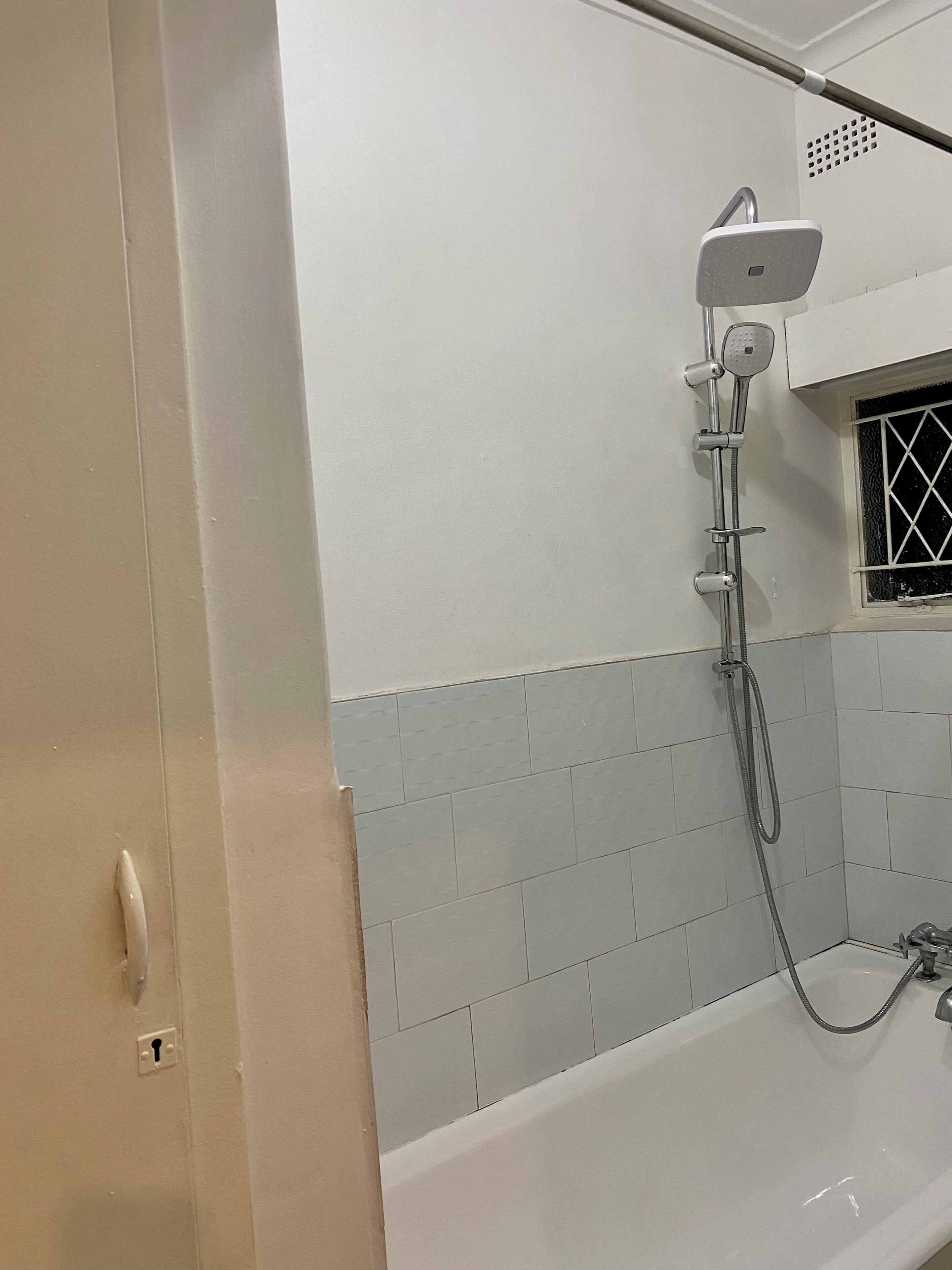 A bathroom with a shower, a bathtub, and a window with a grid pattern.