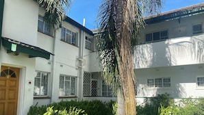 Un edificio con fachada blanca, puertas numeradas y un jardín cuidado con césped y plantas.
