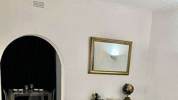 Una sala moderna con un sofá blanco, una mesa de comedor con sillas, una pequeña consola con un globo terráqueo y un espejo en la pared.