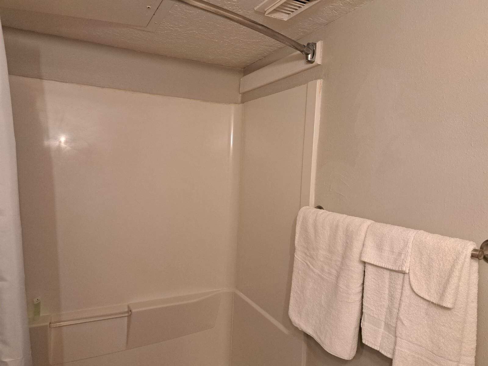 Une salle de bain avec une douche, un porte-serviettes avec une serviette blanche et une poignée de porte bien visible.