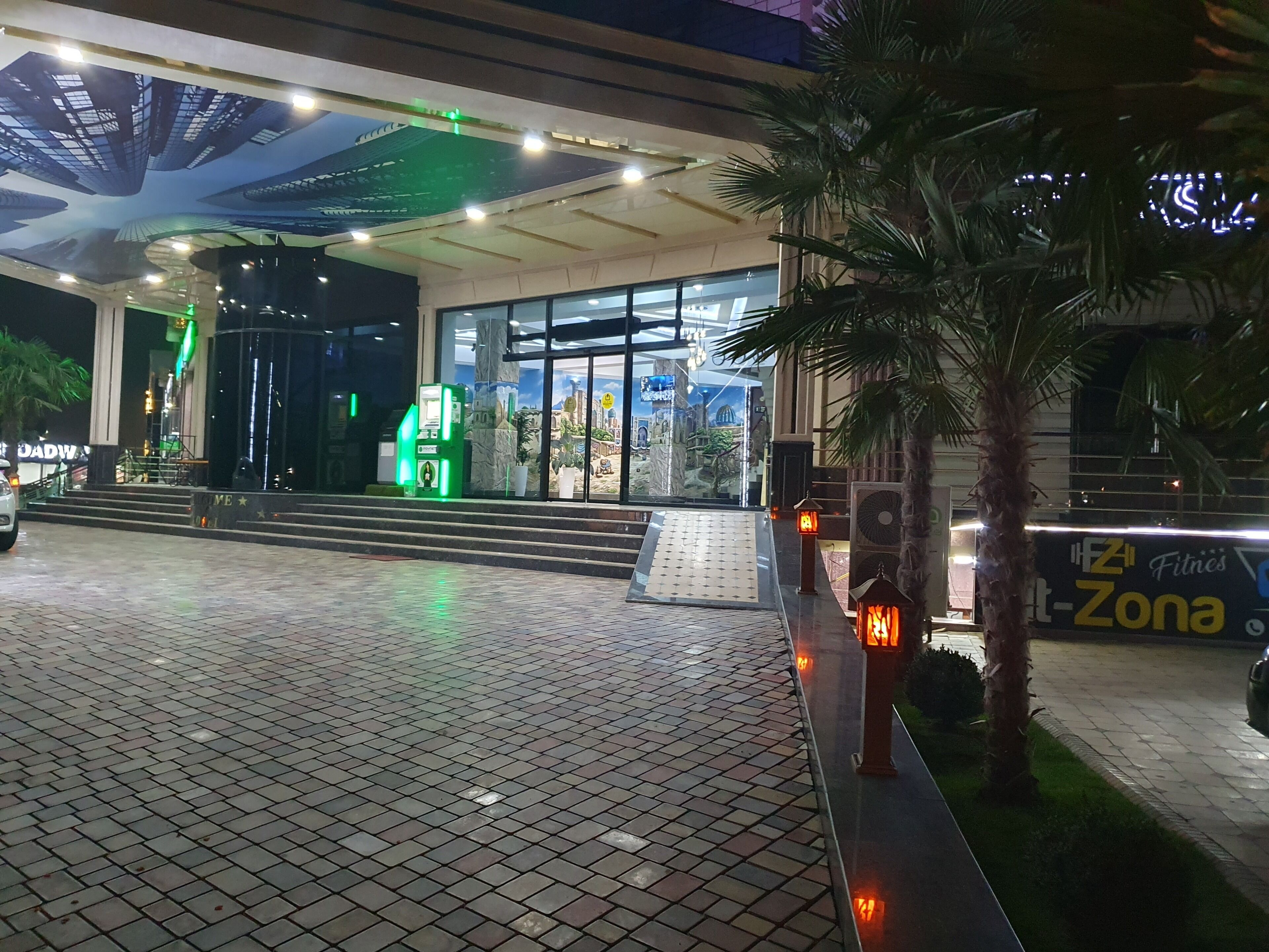 A building entrance with a tiled pavement, a green ATM, and a sign for '4th Fitness Zone'.