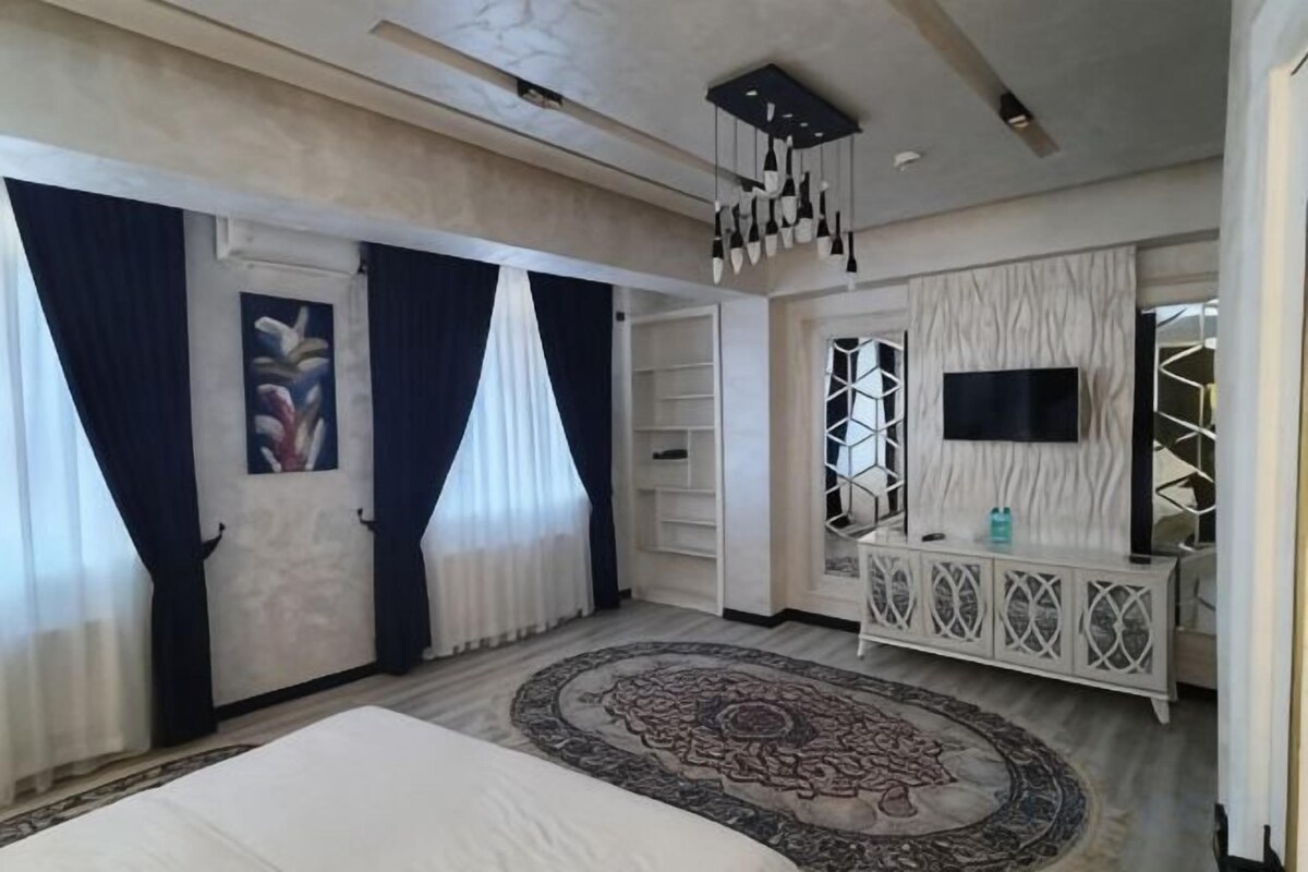 A bedroom with a bed, a TV, a console table, and a patterned rug.