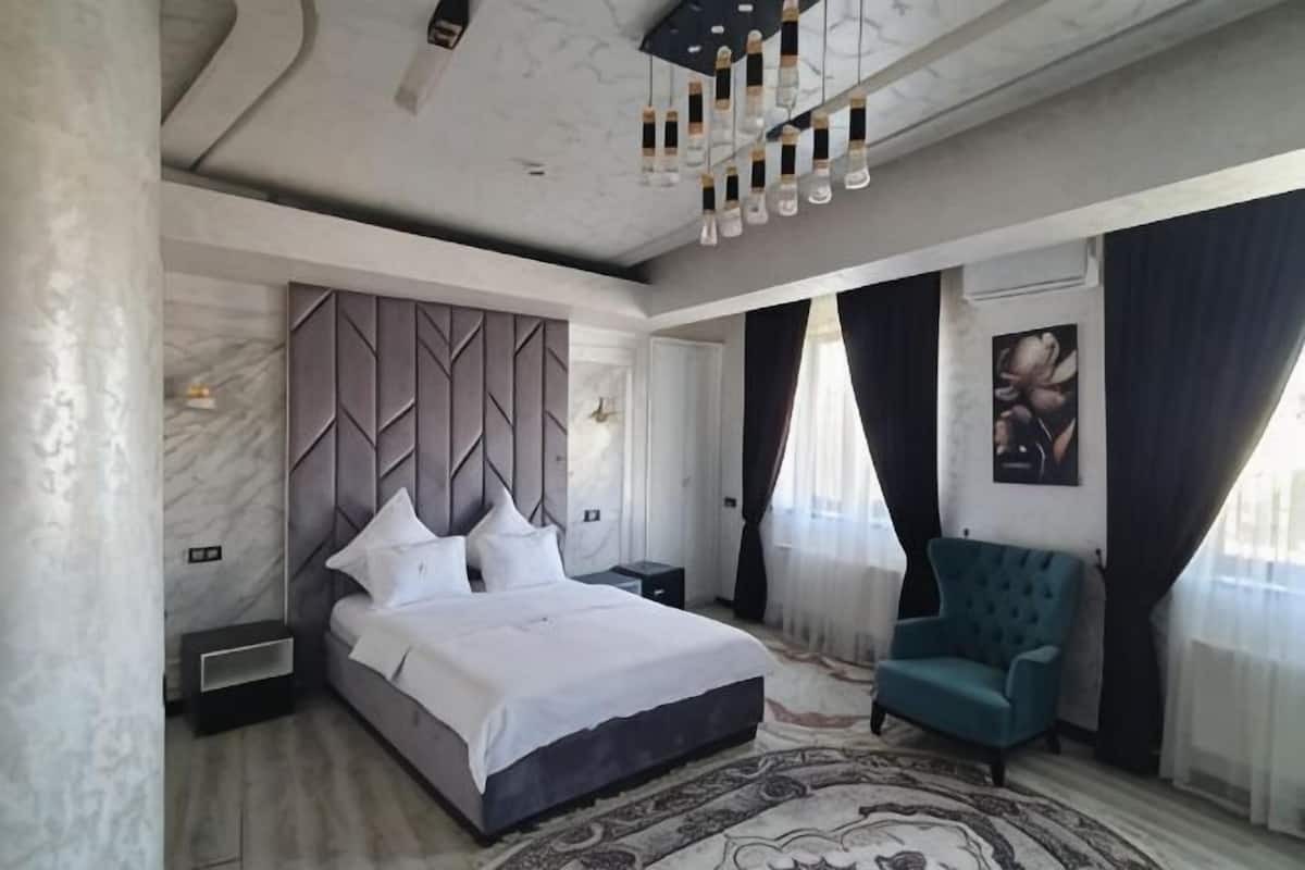 Une chambre à coucher avec un lit, une table de chevet, une chaise et une grande fenêtre avec des rideaux.