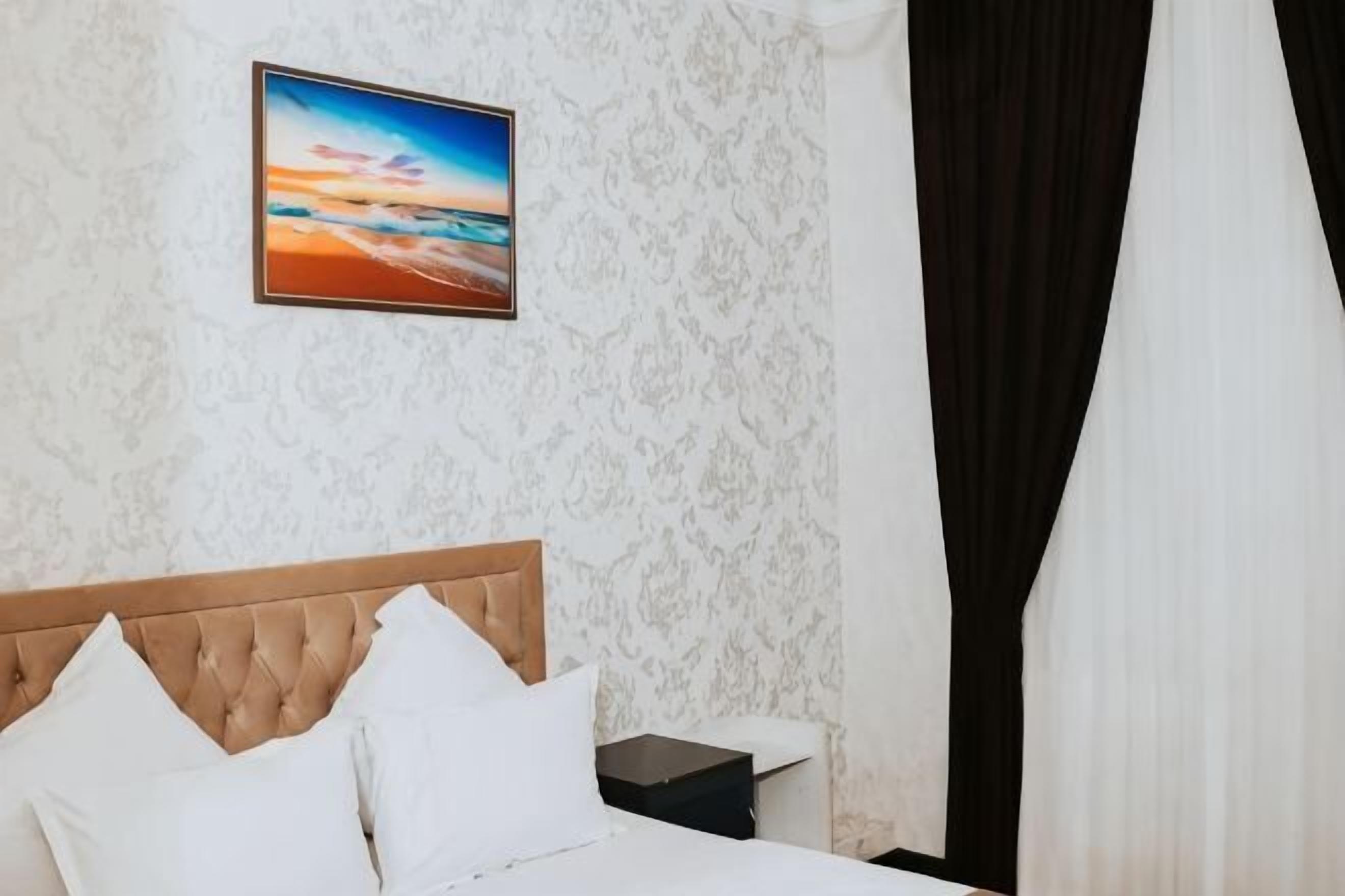 A bedroom with a bed, a nightstand, a framed picture on the wall, and a black curtain.