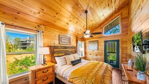 Un dormitorio de cabaña de madera con cama, mesita de noche, lámpara y vistas al exterior.