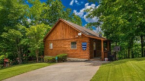A wooden cabin with a porch, surrounded by trees and a clear sky. - Always Together Forever: Make Memories That Last (Sevierville)