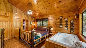 A wooden cabin interior with a bed, a large window, a bathtub, and a ceiling fan. - Always Together Forever: Make Memories That Last (Sevierville)