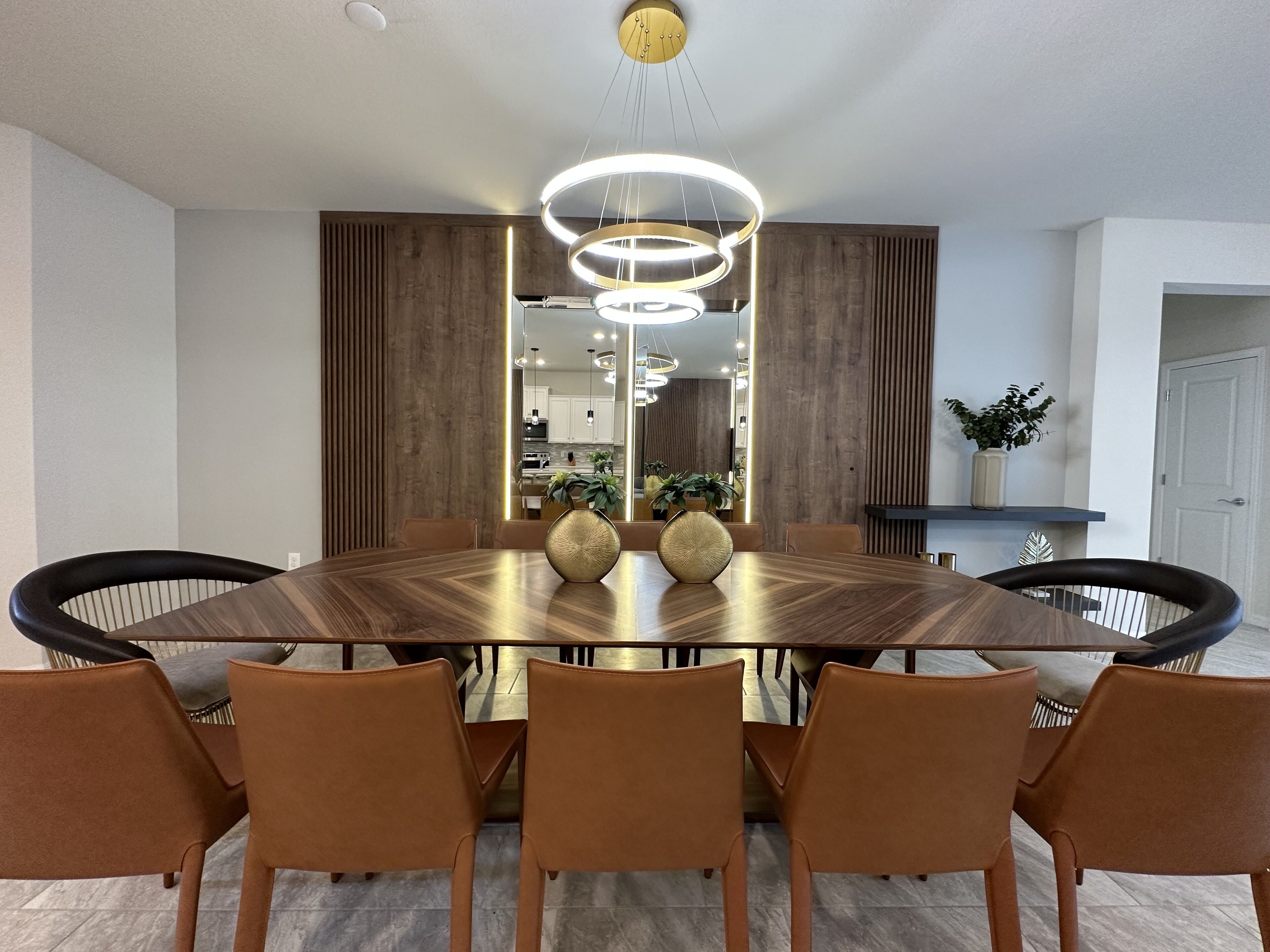 A modern dining room with a large wooden table, brown leather chairs, and a central chandelier.
