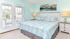 A bedroom with a bed, two bedside tables, a door, and a painting on the wall. - 5 BR Beach House with a Private Pool in Surfside Beach! A Beach Haven (Surfside Beach)