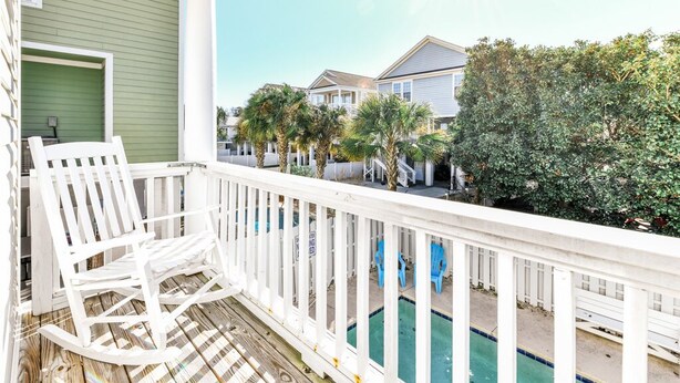 A balcony with a white rocking chair, a pool, and houses in the background. - 5 BR Beach House with a Private Pool in Surfside Beach! A Beach Haven (Surfside Beach)