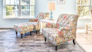 A room with two patterned armchairs, a small table with a lamp, and a view of a porch through a large window. - 5 BR Beach House with a Private Pool in Surfside Beach! A Beach Haven (Surfside Beach)