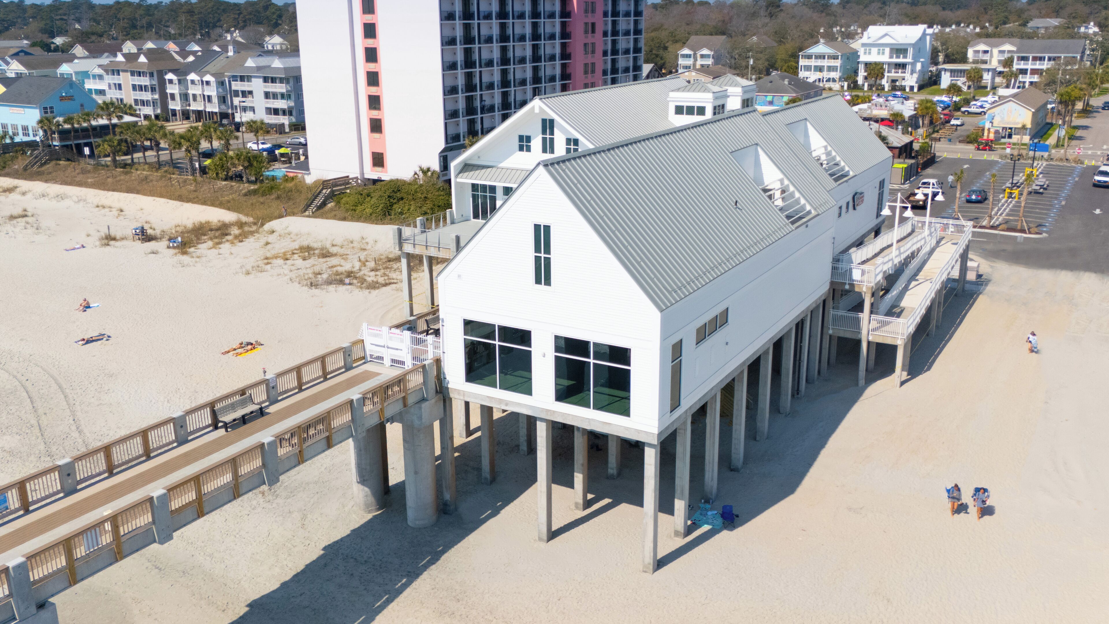 A beachfront building with a flat roof, large windows, and a wooden deck extending onto the beach.