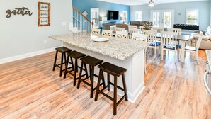 A spacious kitchen with a central island, wooden bar stools, and a blue accent wall. - 7 BR 2nd Row Beach House with a Private Pool! Aquadisiac  (Surfside Beach)