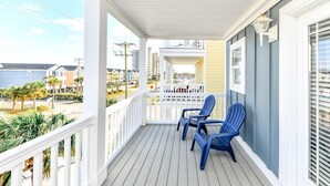 A covered porch with white railings, two blue Adirondack chairs, and a view of the beach and neighboring houses. - 7 BR 2nd Row Beach House with a Private Pool! Aquadisiac  (Surfside Beach)