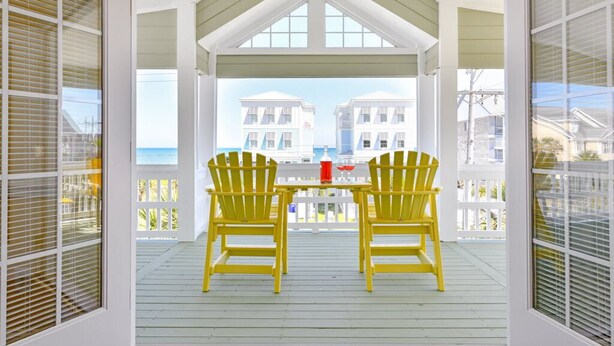 A covered porch with two yellow Adirondack chairs and a table, overlooking a beach with buildings in the background. - 5 BR 2nd Row Beach House with a Private Pool! Beach Dreams (Surfside Beach)