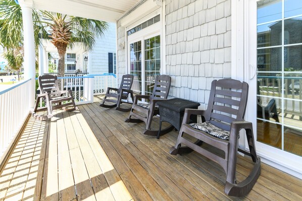 A wooden deck with outdoor furniture, including chairs and a table, and a white building with large windows in the background.