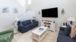 Una sala de estar con un sofá azul, un sofá verde, una mesita de centro, un televisor y obras de arte en la pared.