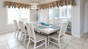 Comedor con una mesa blanca, seis sillas, un cartel de 'Welcome' y un valance estampado sobre las ventanas.