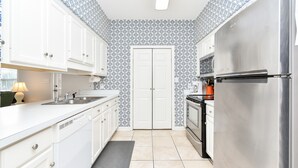 Una cocina moderna con armarios blancos, un refrigerador de acero inoxidable y papel tapiz estampado.