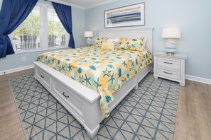Une chambre à coucher avec un lit, deux tables de chevet, une fenêtre avec des rideaux et un tableau au mur.