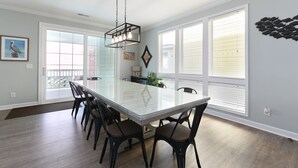 A spacious dining area with a large table and chairs, large windows, and a view of the outdoors.