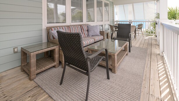 A covered porch with wicker furniture, a glass-top table, and a cushioned sofa.