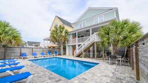 A swimming pool with lounge chairs, a covered patio, and a multi-story building with a balcony.