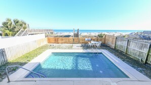 Una piscina amb una terrassa de fusta, una tanca de fusta i vista a la platja.