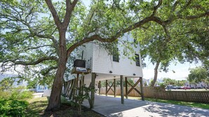 A treehouse with a wooden deck and a small porch, surrounded by lush greenery. - 4 BR Beach House with a Private Pool! It's A Stone Harbor Thing (Surfside Beach)