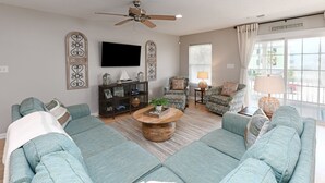 A spacious living room with a sectional sofa, a coffee table, and a television mounted on the wall. - 2nd Row 5 BR Beach House with a Private Pool! Sale Away (Surfside Beach)