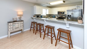 A modern kitchen with a central island, bar stools, a refrigerator, and a microwave. - 2nd Row 5 BR Beach House with a Private Pool! Sale Away (Surfside Beach)