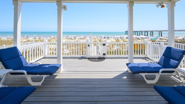 A covered deck with two blue lounge chairs and a view of a beach and pier. - Oceanfront 5 BR Beach House with a Private Pool! La Dolce Vita (Surfside Beach)