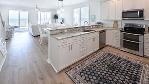 A modern kitchen with white cabinets, a large island, stainless steel appliances, and a view to the outside. - Oceanfront 5 BR Beach House with a Private Pool! La Dolce Vita (Surfside Beach)