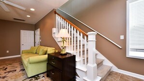Un escalier avec des balustrades blanches, un canapé vert et une table de chevet en bois foncé avec une lampe.