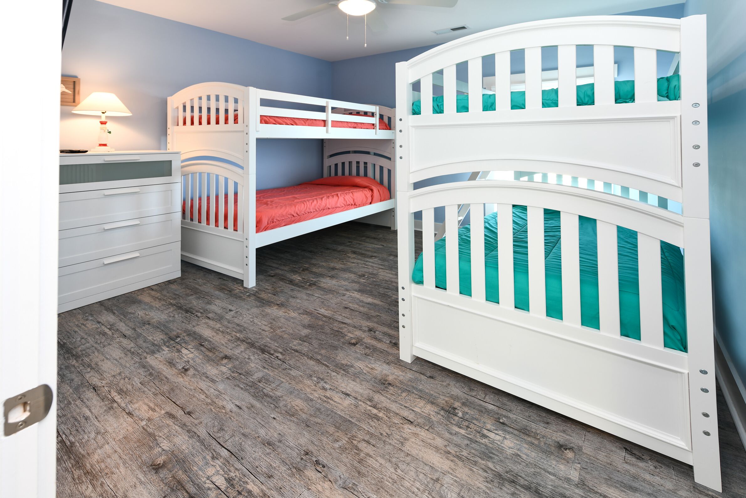 A room with two bunk beds, a white dresser, and a ceiling fan.